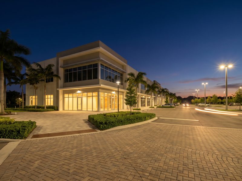 Low-rise South Florida commercial building with storefront and parking lot lighting at dusk